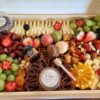 Maison (Serves 4–6): Includes 3–4 artisanal cheeses, 2 cured meats, fresh fruit, nuts, honey and jam, olives, a sweet treat, and crackers. Tray or container is subject to availability and may vary in shape and material. Wooden boards available for rent.